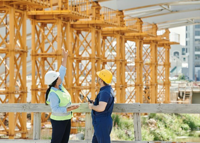 Two engineers in hardhats discuss projects at a busy construction site.